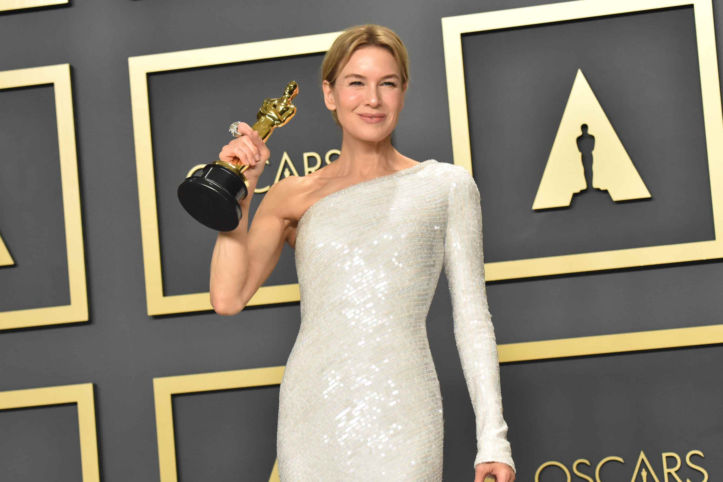 Renée Zellweger hält ihren Oscar für „Judy“ in einem weißen One-Shoulder-Kleid