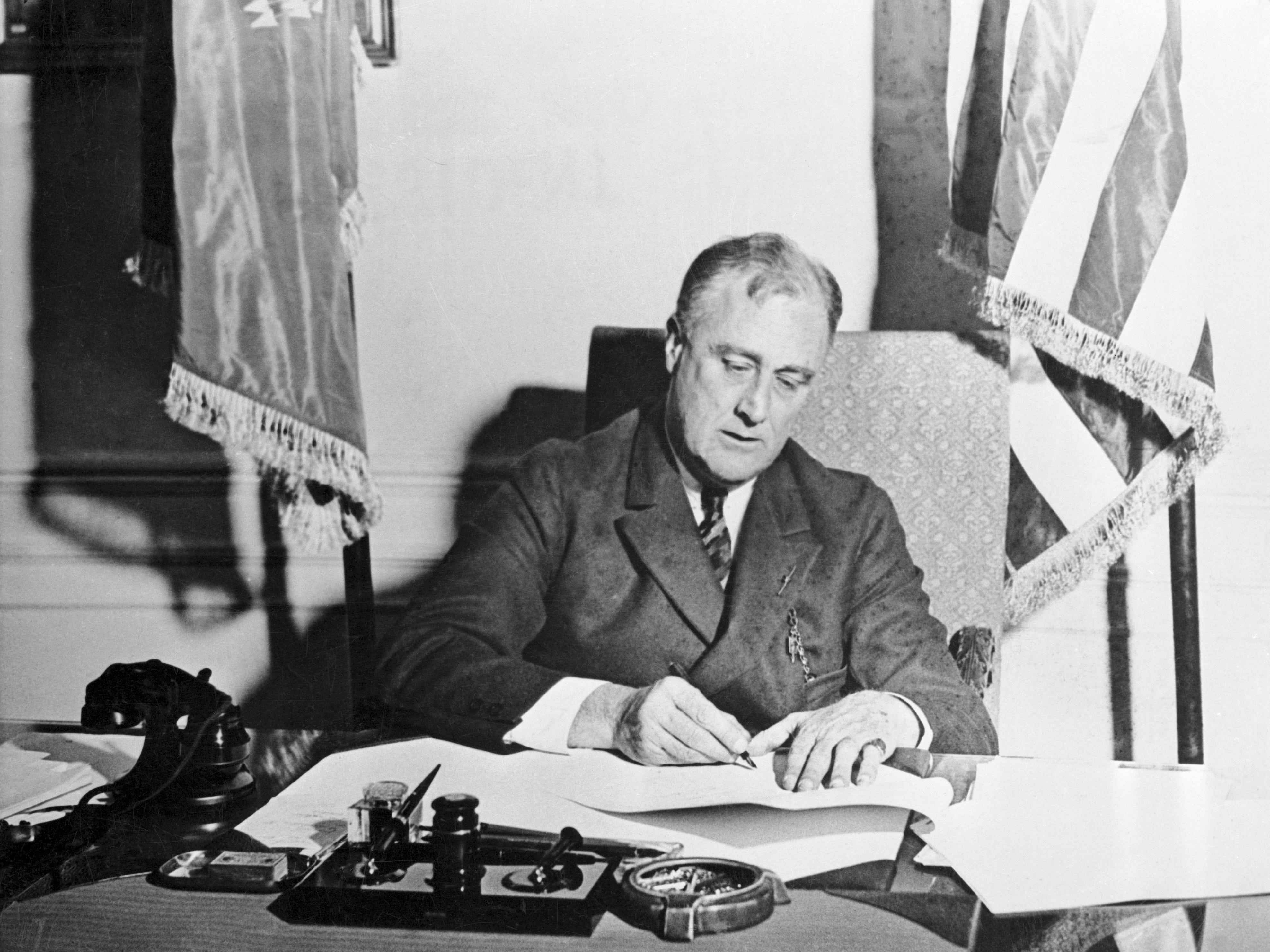 Franklin Delano Roosevelt unterschreibt Papiere an seinem Schreibtisch.