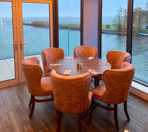 Ein Esstisch neben raumhohen Fenstern mit Blick auf einen großen See.
