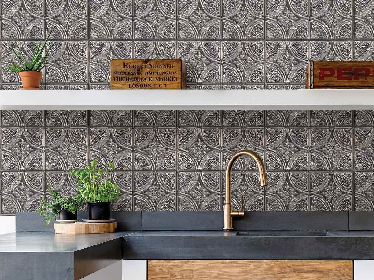 Ein silberner Backsplash mit einem komplizierten Scroll-Design bedeckt die Wand hinter einer Küchenspüle.