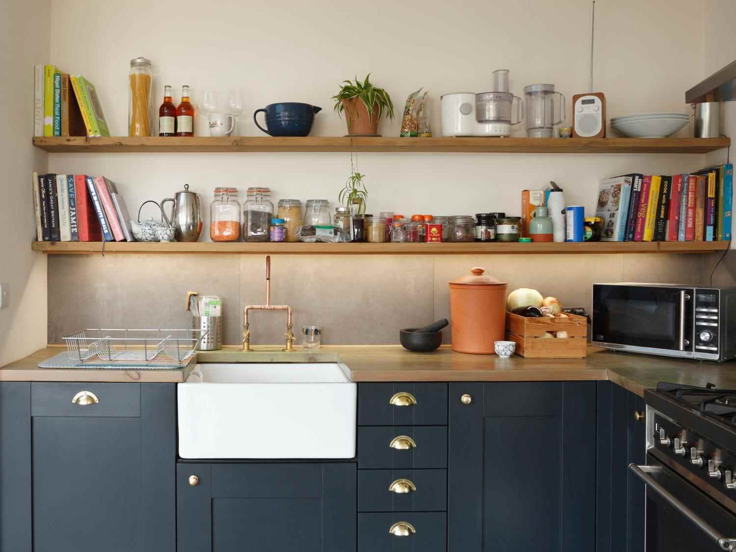 Eine Küche mit marineblauen Schränken und goldenen Griffen mit Holzregalen an den Wänden, die mit Büchern und Küchengeräten gefüllt sind.