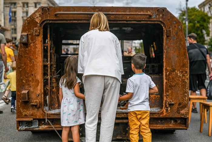 Eine Frau und zwei kleine Kinder schauen durch die Rückseite eines zerstörten russischen Panzerfahrzeugs in der historischen Khreschatyk-Straße in Kiew.