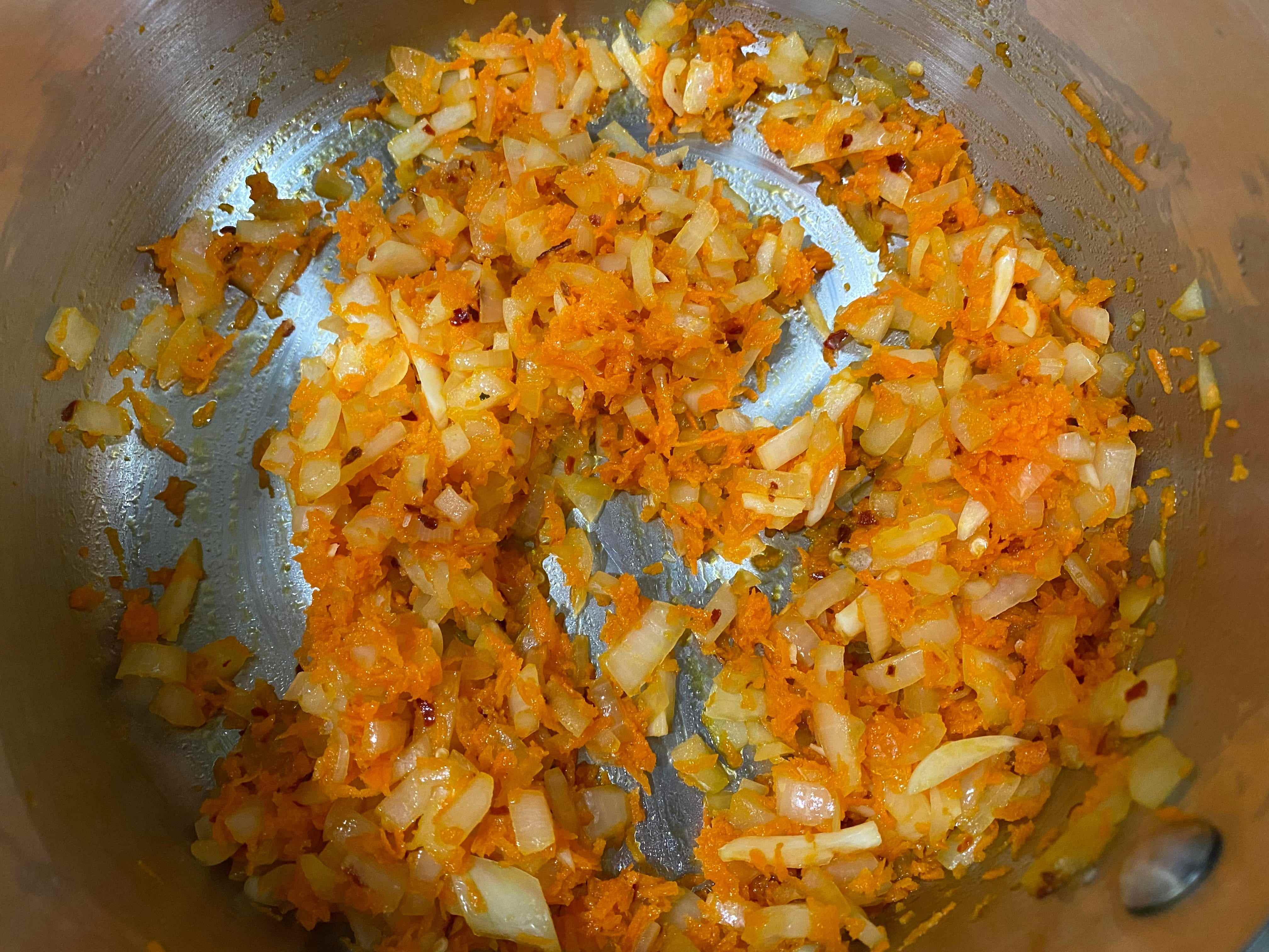 Zwiebel, Knoblauch und geraspelte Karotten in einer Pfanne anbraten