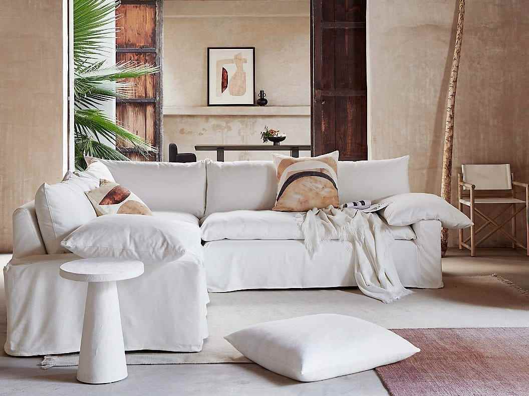 Ein weißes Crate & Barrel Ever Sofa sitzt auf geschichteten Teppichen und hat mehrere Wurfkissen und eine Decke darüber drapiert.