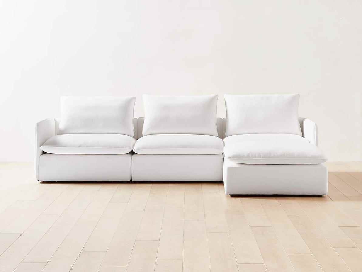 Ein weißes CB2 Lumin Sofa steht auf einem Holzboden in einem ansonsten leeren Raum.