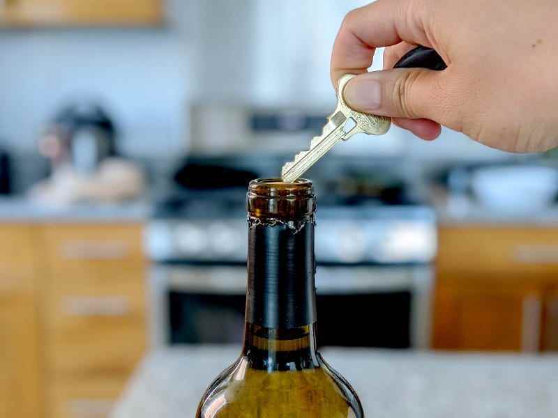 Eine Hand hält einen Hausschlüssel an der Spitze eines Weinflaschenkorkens, um zu demonstrieren, wie man eine Weinflasche ohne Korkenzieher 2022 öffnet.