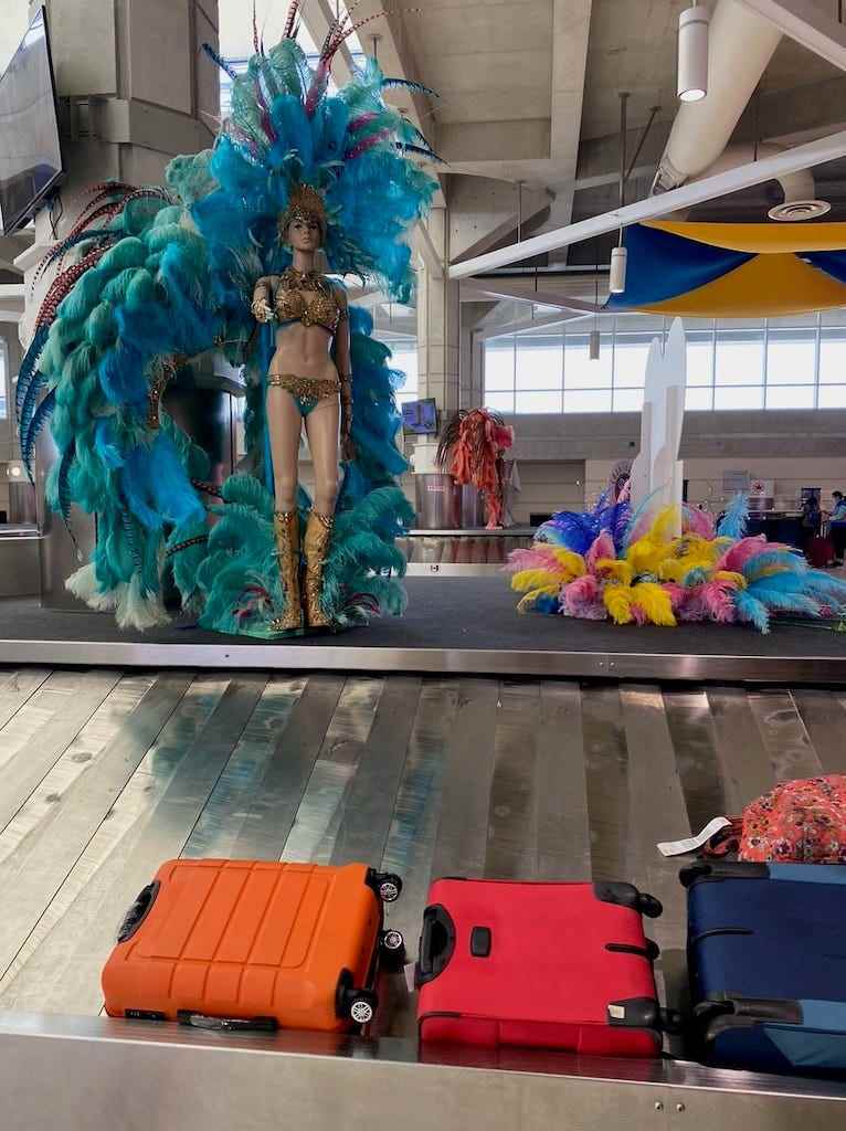 Gepäck, das auf einem Flughafenband mit einer mit Federn geschmückten Schaufensterpuppe für Carnevale ankommt.