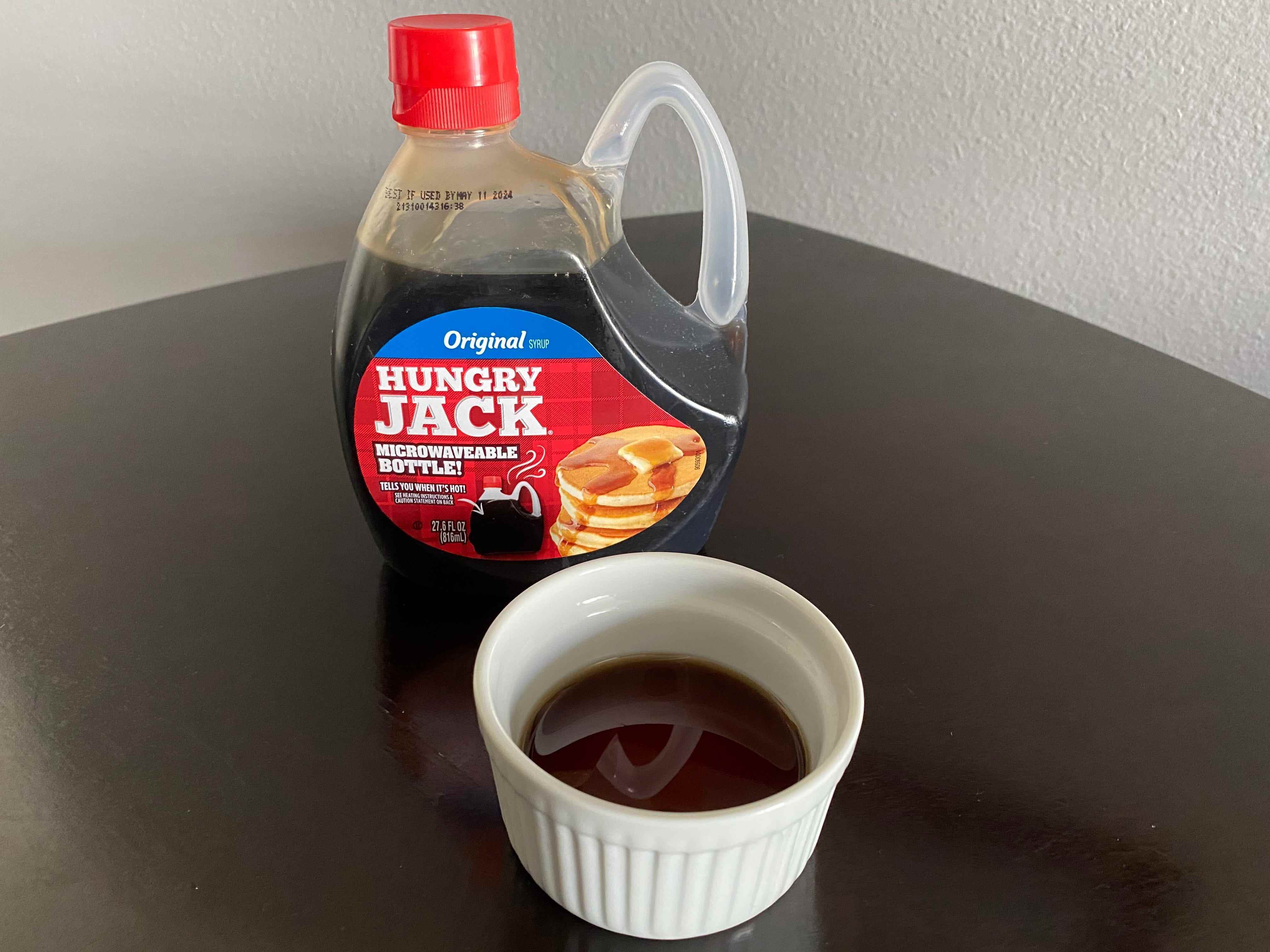 eine Flasche hungrigen Jack-Pancake-Sirup neben einem weißen Auflaufförmchen, das mit dem Sirup gefüllt ist