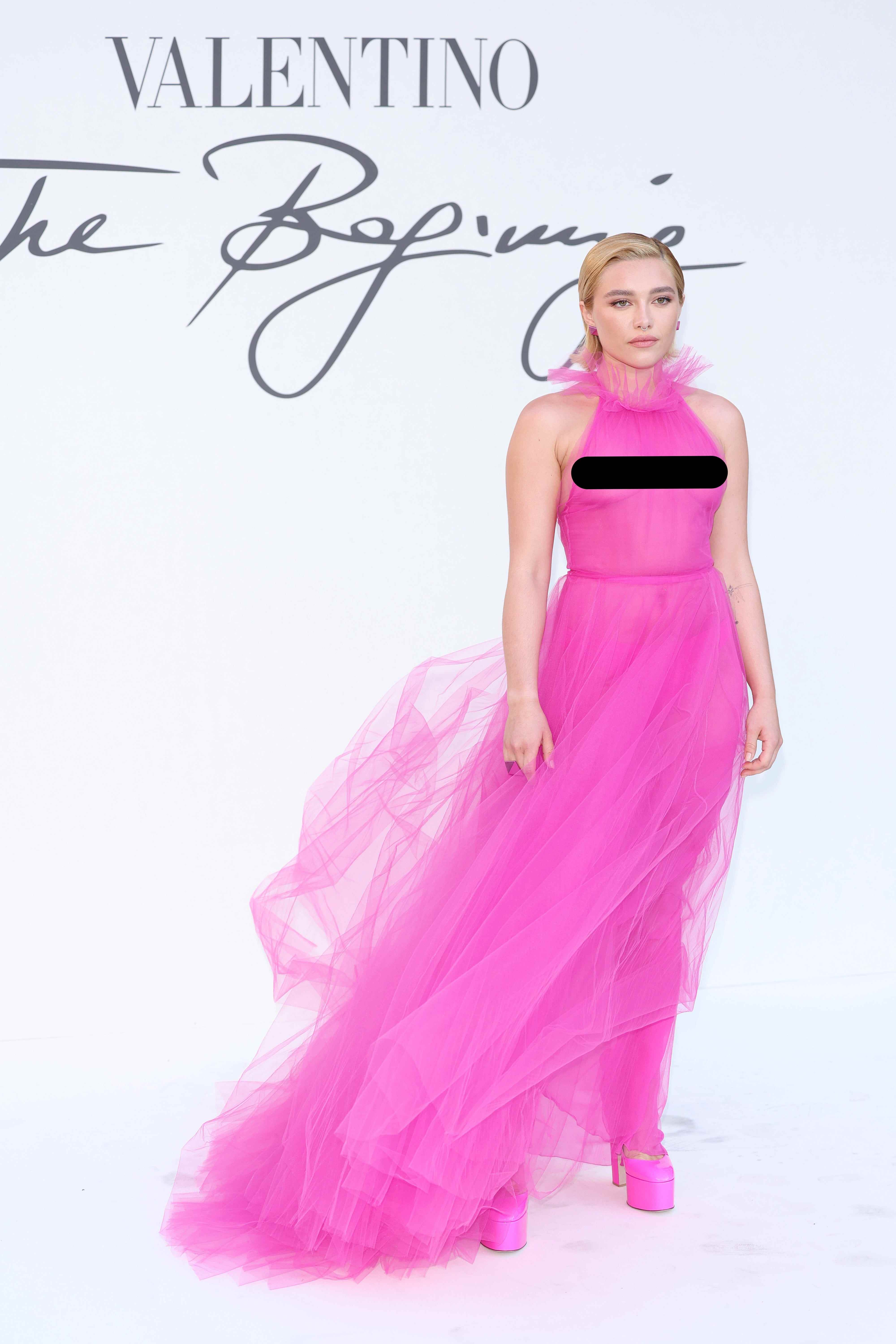 Florence Pugh steht in einem rosafarbenen, transparenten Kleid vor einer weißen Kulisse.