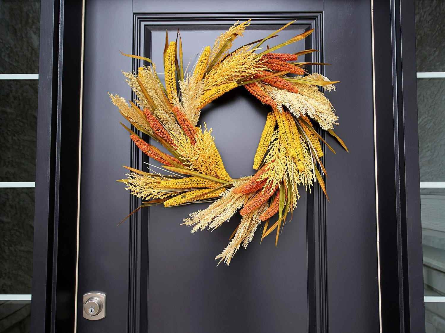 Ein beiger, gelber und orangefarbener Weizen- und Graskranz hängt an einer schwarzen Tür.