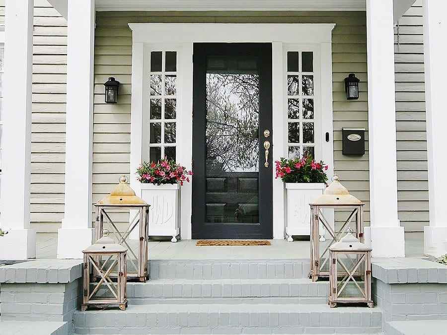 Die vordere Veranda eines beigefarbenen Hauses wird gezeigt und die Haustür ist schwarz.