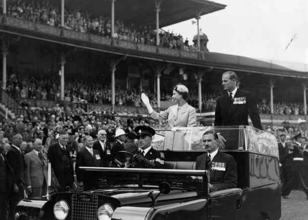 Königin Elizabeth II. und Prinz Philip winken am 25. Februar der Menge zu, als sie während ihrer Australien-Tour 1954 auf einer Rennstrecke des Melbourne Cricket Ground gefahren werden.