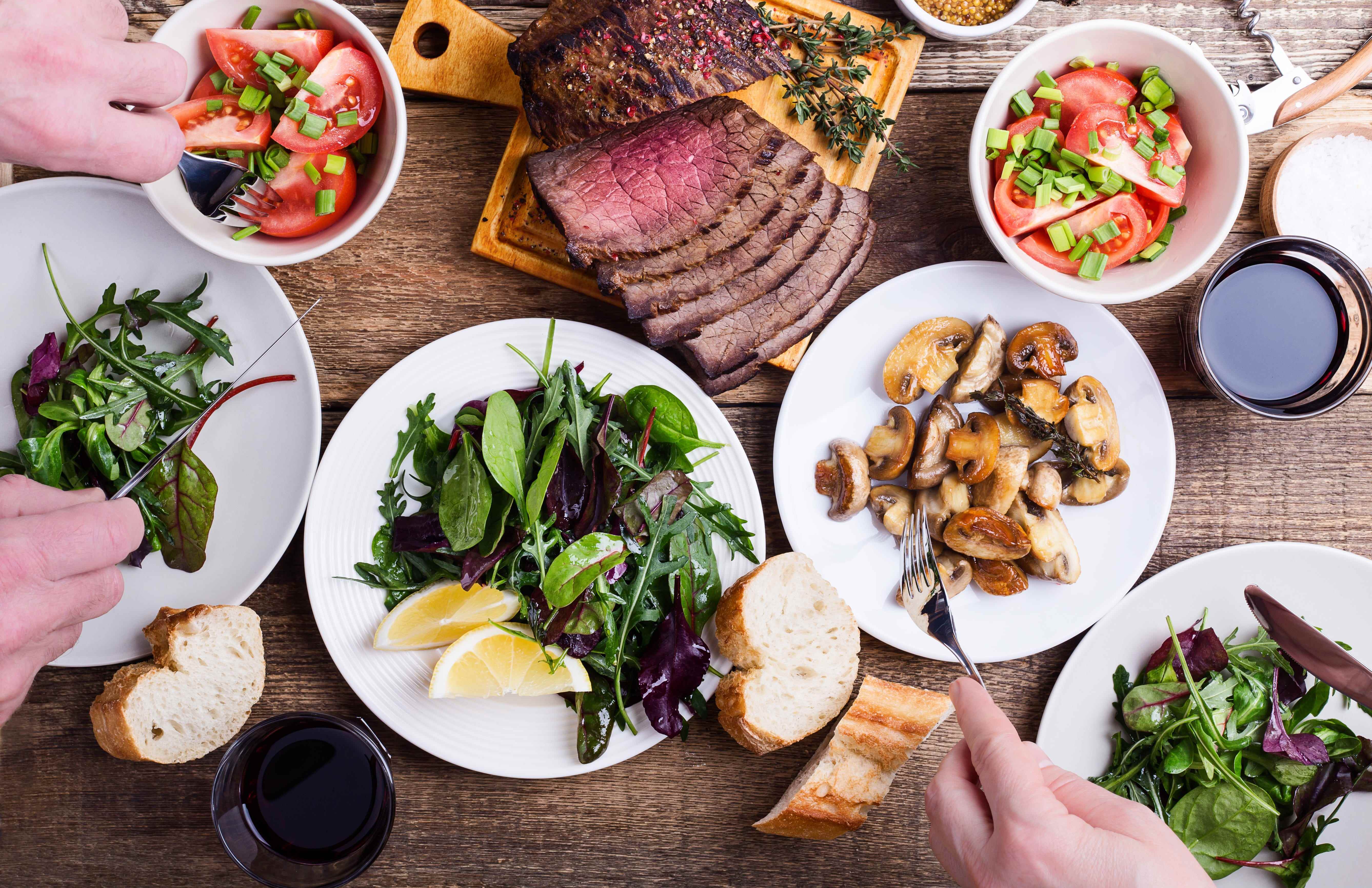 Tablescape mit Salaten, Steak, Pilzen und Brot