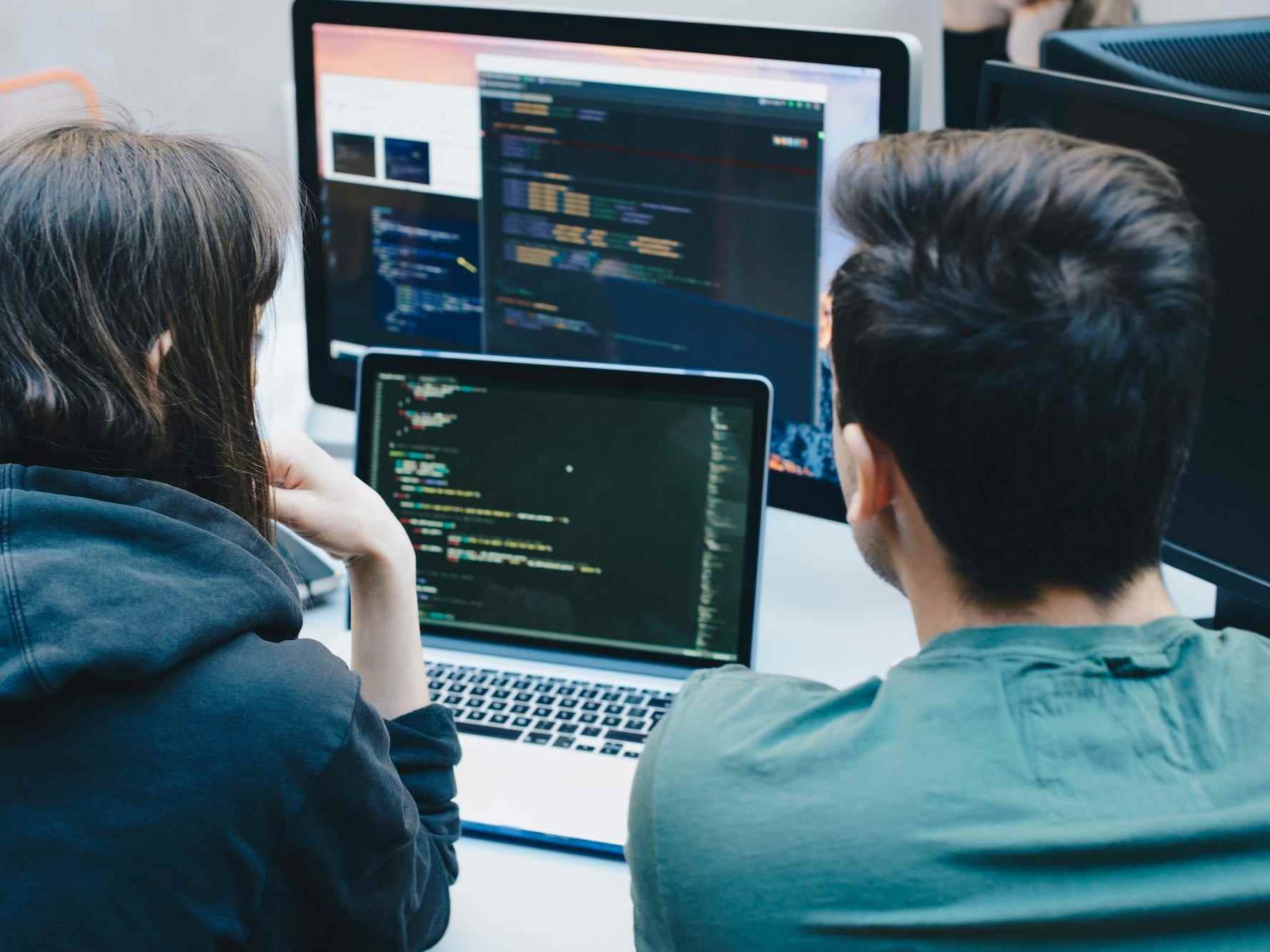 Zwei Personen betrachten Code auf einem Laptop und einem Computer