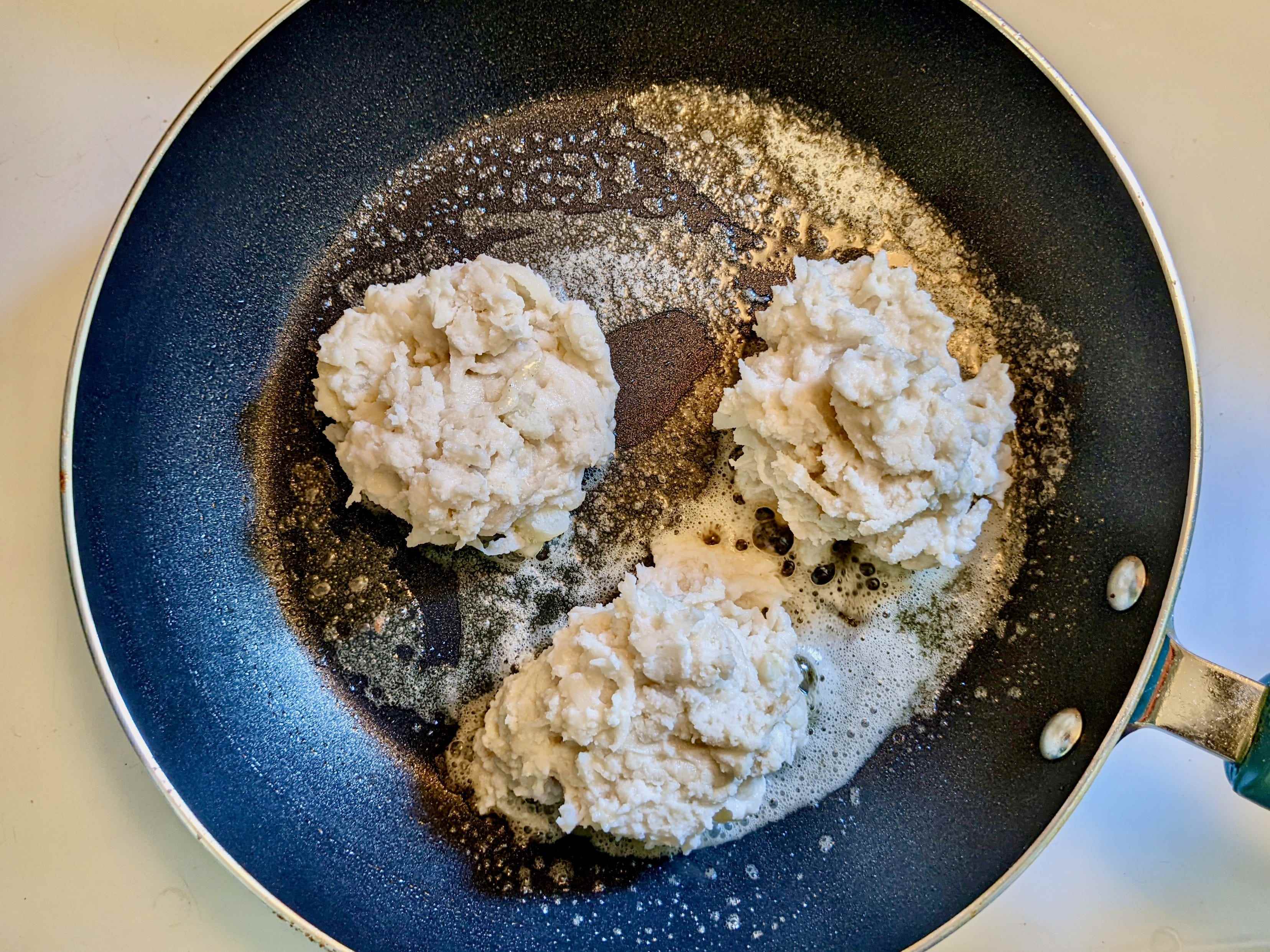 Drei Kugeln Kartoffelmischung in einer Bratpfanne mit Butter