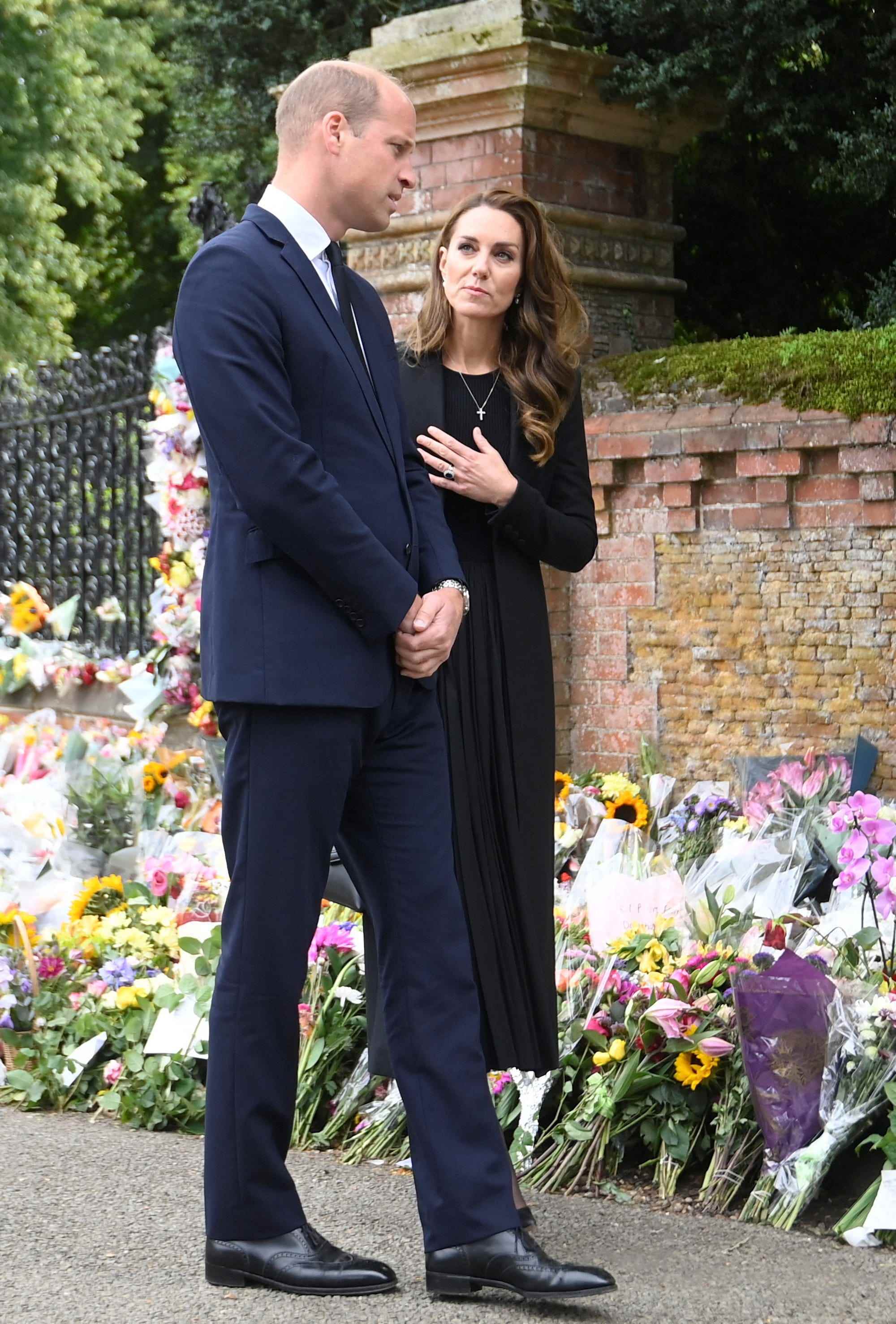 Kate Middleton sieht Prinz William mit ihrer Hand auf ihrem Herzen an, während sie vor Blumen stehen.