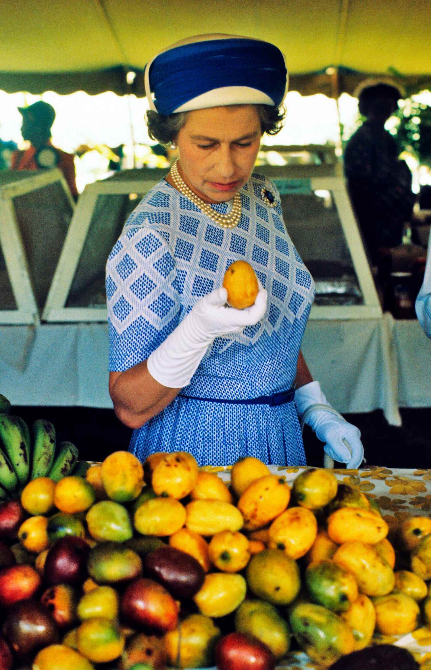 Königin Elizabeth II. hebt eine Mango auf, als sie im Oktober 1977 einen Markt auf den Britischen Jungferninseln besichtigt.