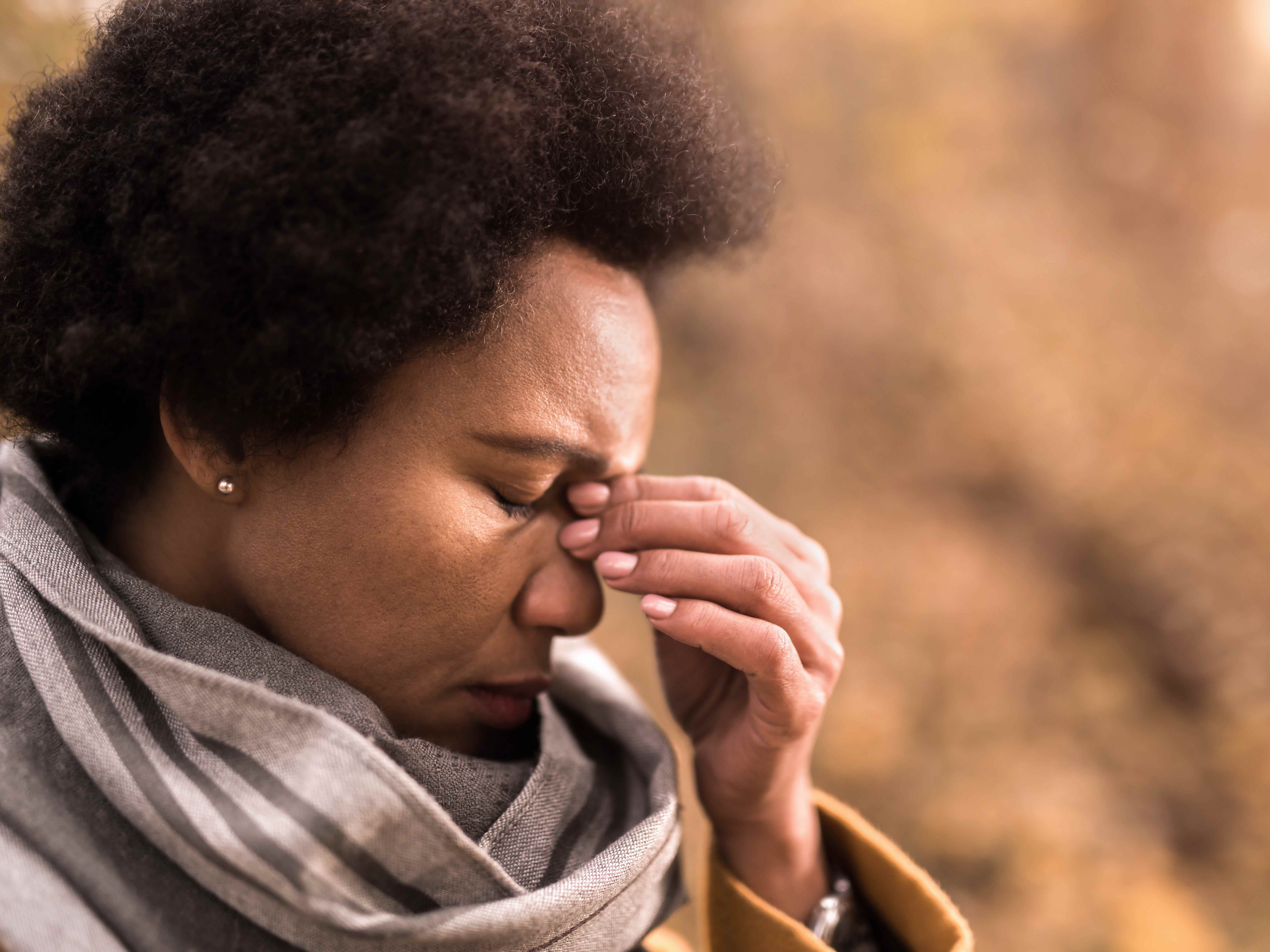 Nahaufnahme einer erwachsenen afroamerikanischen Frau, die am Herbsttag im Freien Kopfschmerzen hat.