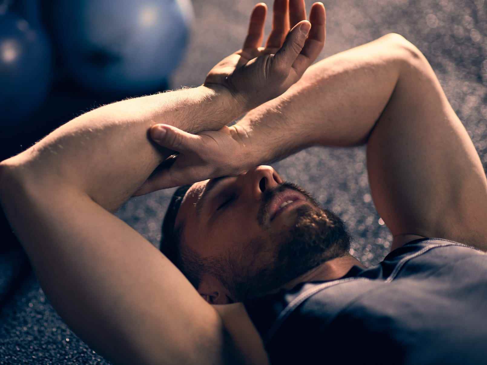 Ein müder Athlet, der sich nach dem Training erschöpft neben Kettlebell-Gewichte auf den Boden eines Fitnessstudios legt