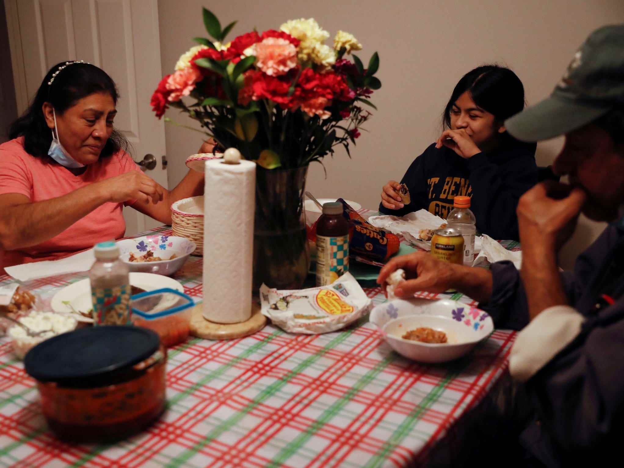 Zwei Erwachsene und ein Kind essen an einem Tisch mit Papptellern und Blumenstrauß zu Abend