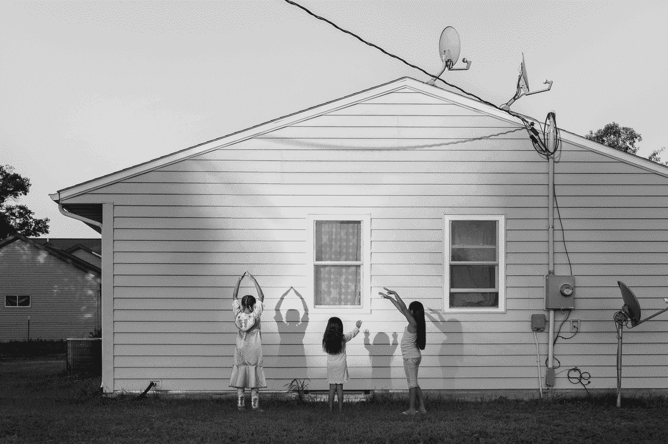 Drei junge Mädchen machen Schatten an der Seite eines Holzhauses