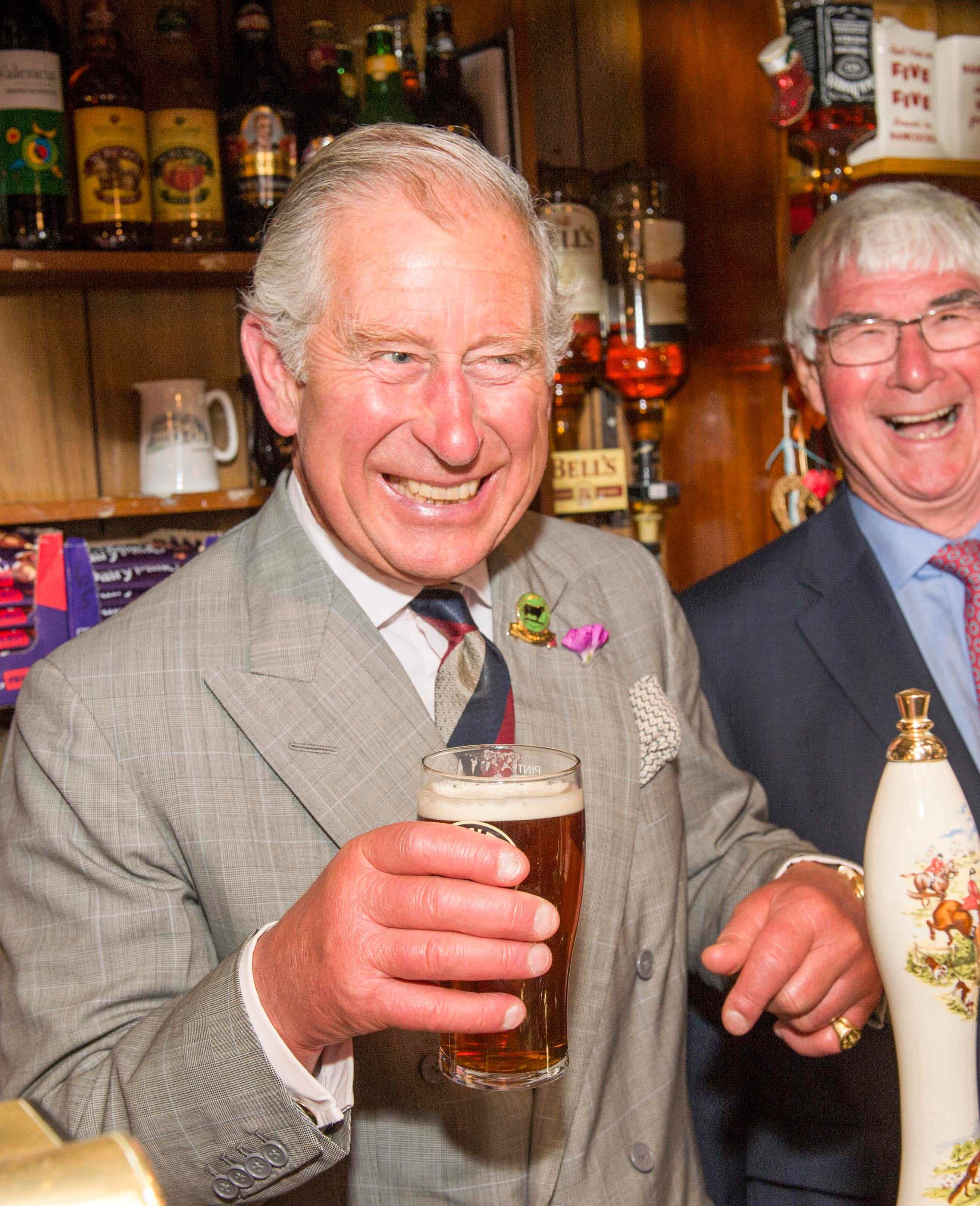 König Charles lächelt und hält 2015 in Talgarreg, Wales, ein Pint Bier in der Hand.