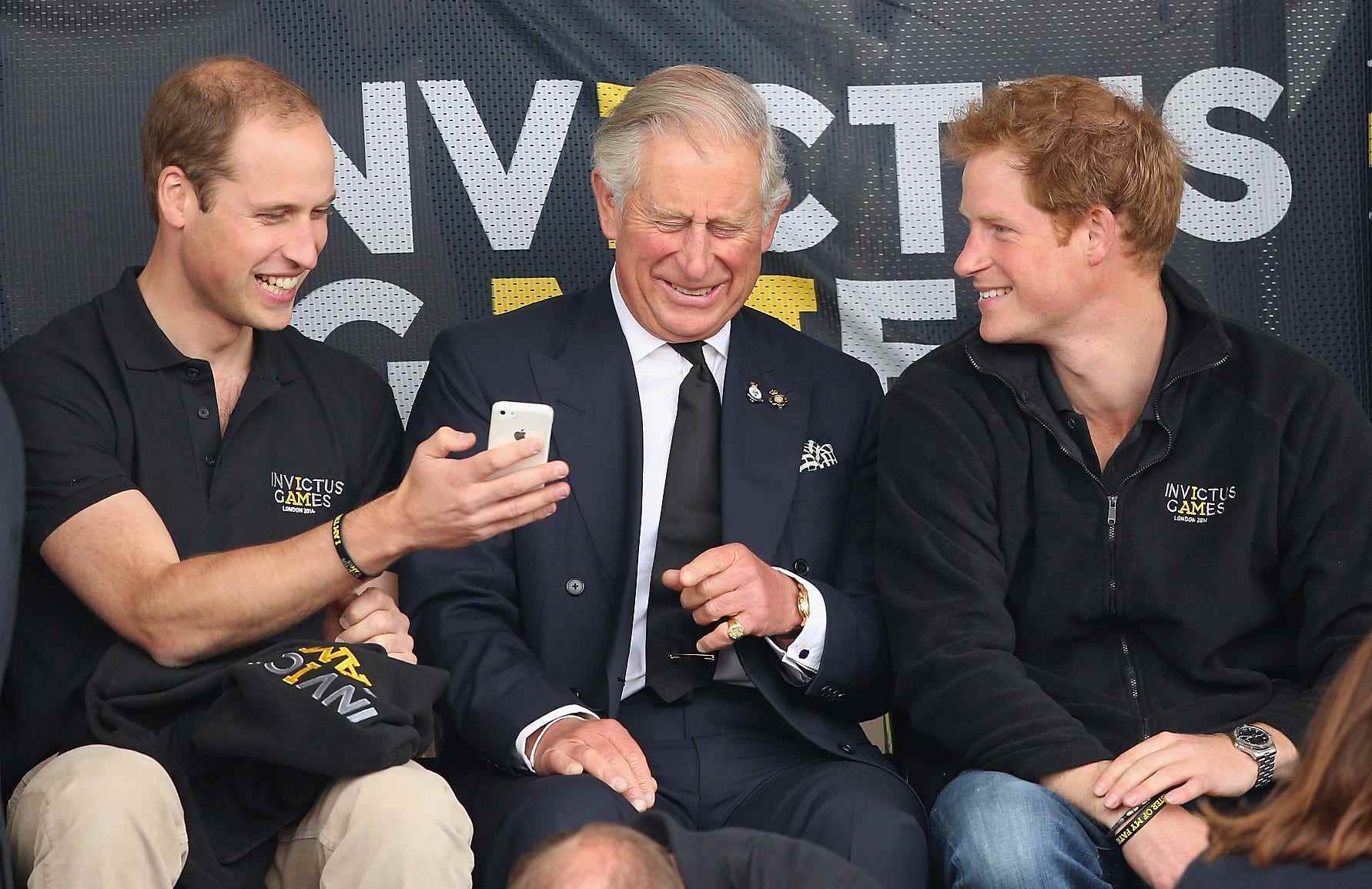 Prinz William zeigt König Charles und Prinz Harry bei den Invictus Games 2014 sein Telefon.