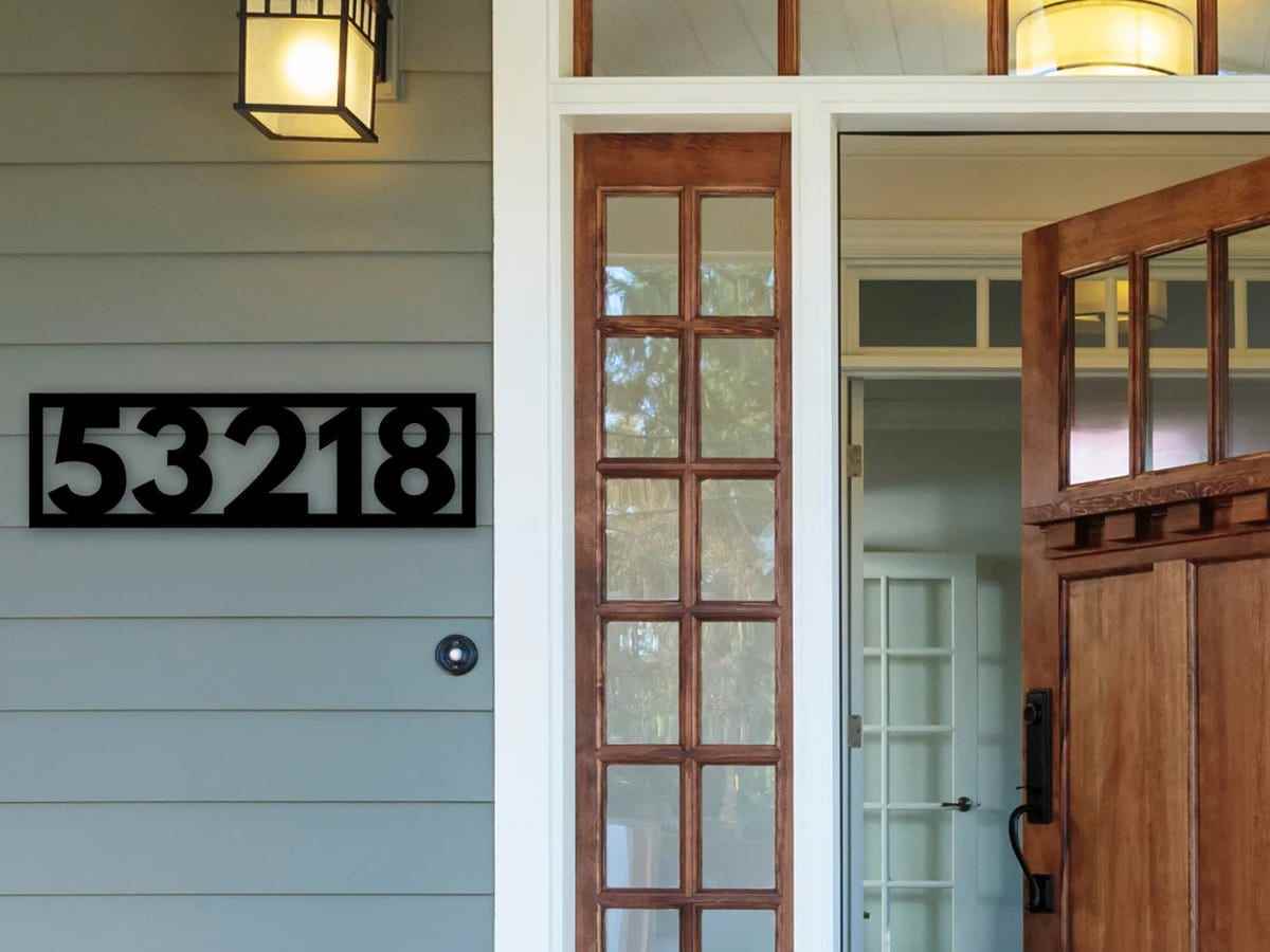 Die kräftigen schwarzen Hausnummern 53218 sind in ein schwarzes Rechteck eingerahmt und auf einem grüngrauen Hausanschluss neben einer Haustür montiert.