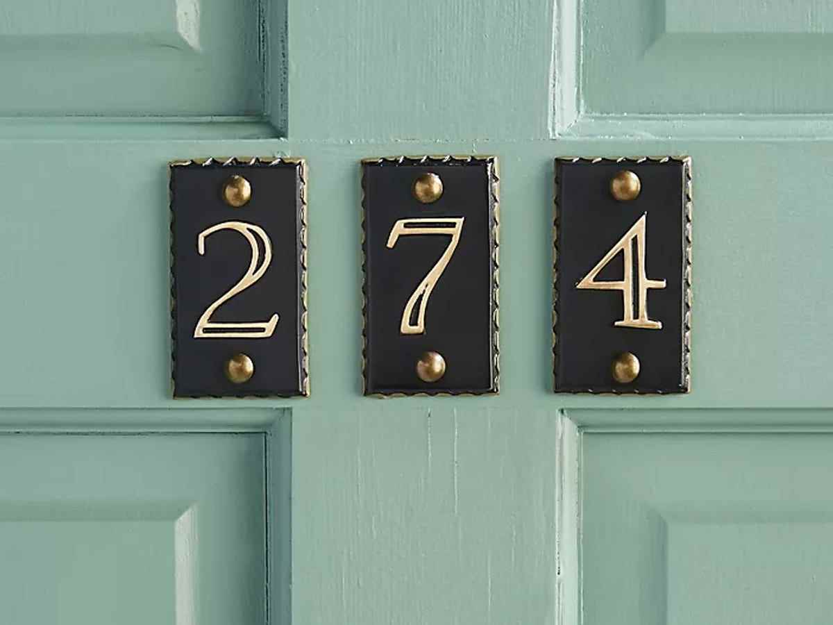 Schwarze individuelle Nummernschilder 2, 7 und 4 mit goldener Nummerierung und Umrandung sind an einer aquafarbenen Haustür angebracht.