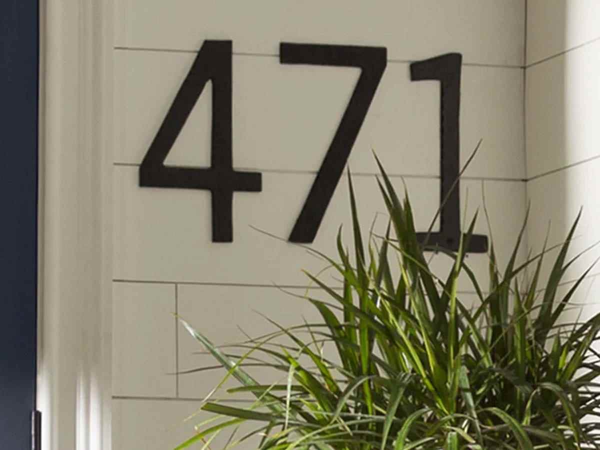Hausnummern mit schwarzen Serifen werden horizontal auf weißen Seitenwänden eines Hauses angebracht.