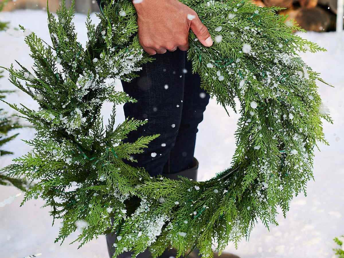 Ein Imitat-Zypressenkranz, der von einer Hand in einem schneebedeckten Hintergrund gehalten wird