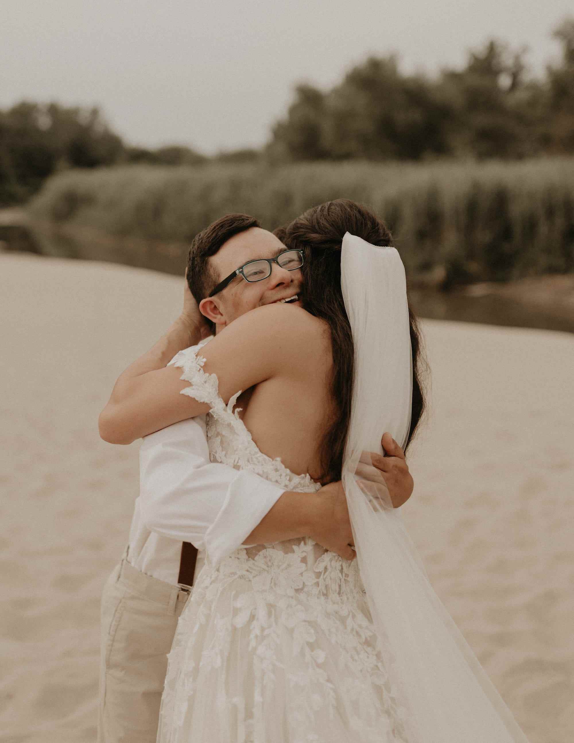 Ein Bruder umarmt seine Schwester, die ein Hochzeitskleid trägt, am Strand.