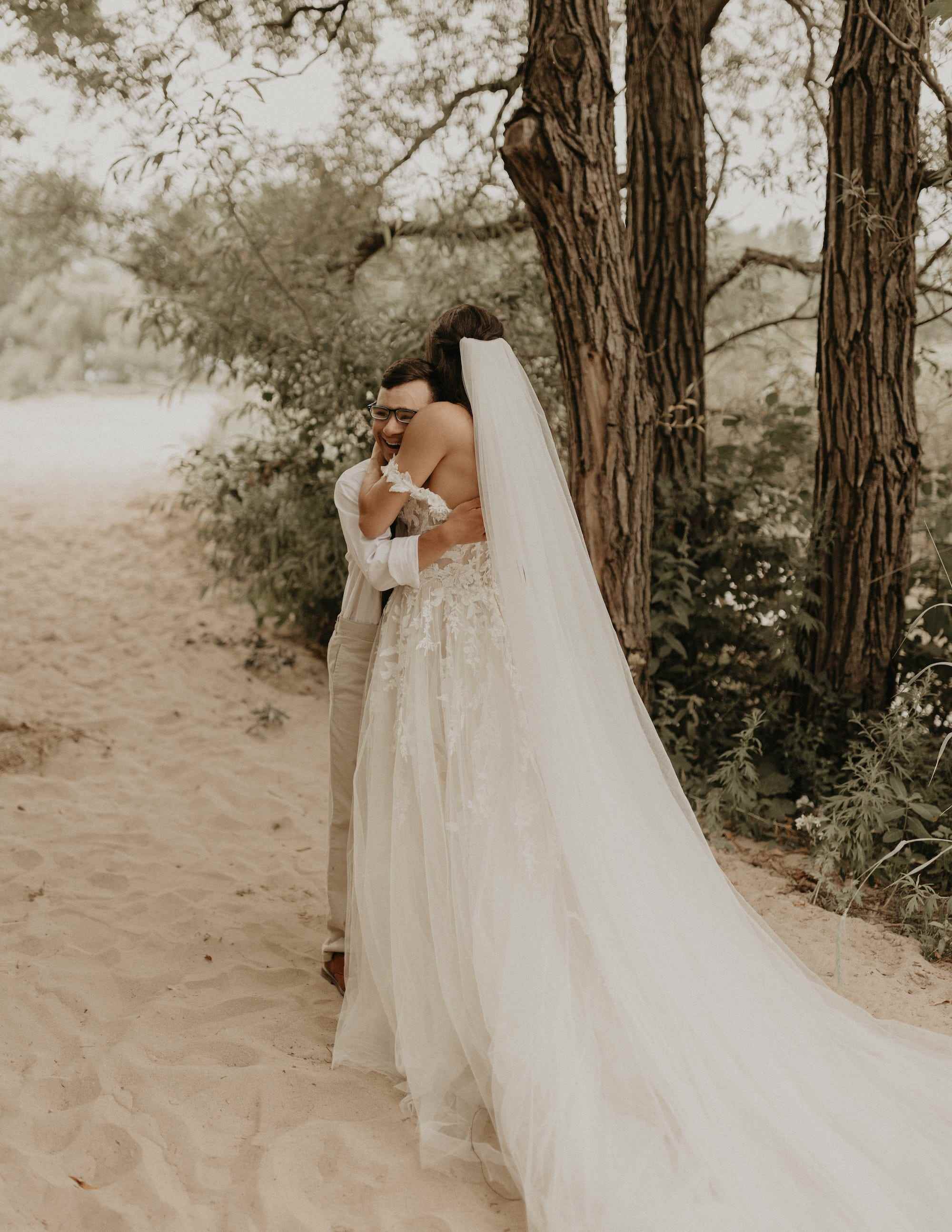 Eine Braut und ihr Bruder umarmen sich in Hochzeitskleidung am Strand.