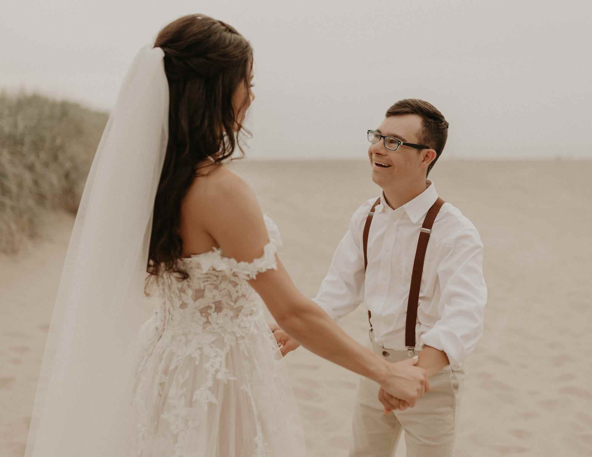 Eine Braut und ihr Bruder halten Händchen am Strand.