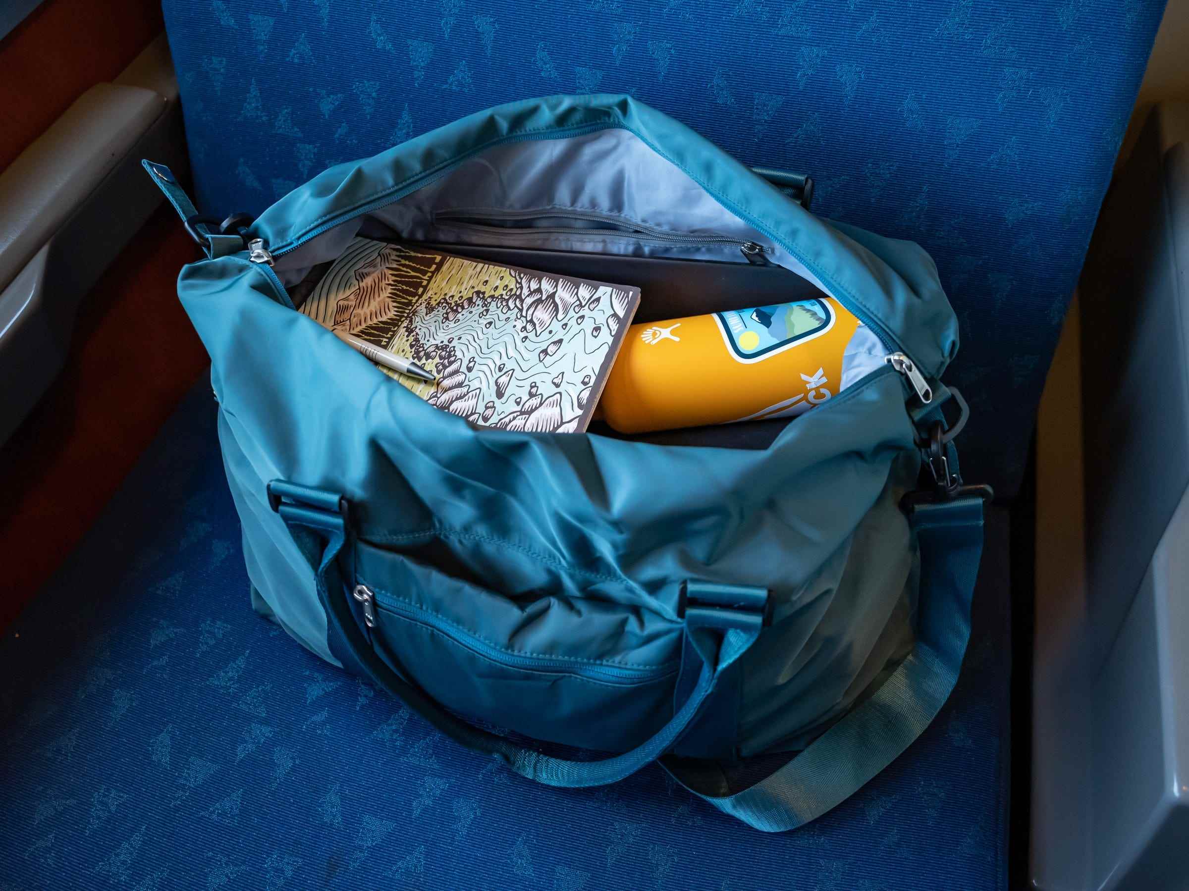Blaue Reisetasche gefüllt mit Snacks und orangefarbener Wasserflasche auf einem blauen Amtrak-Sitz