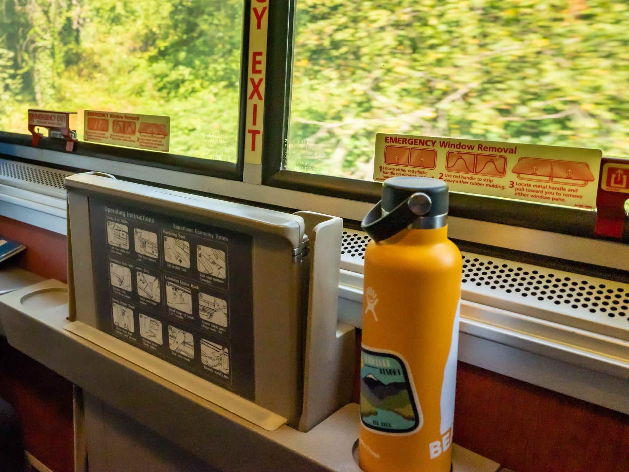 Blick auf Bäume außerhalb des Fensters mit orangefarbener Wasserflasche auf dem Sims am Fenster im Amtrak-Schlafwagen