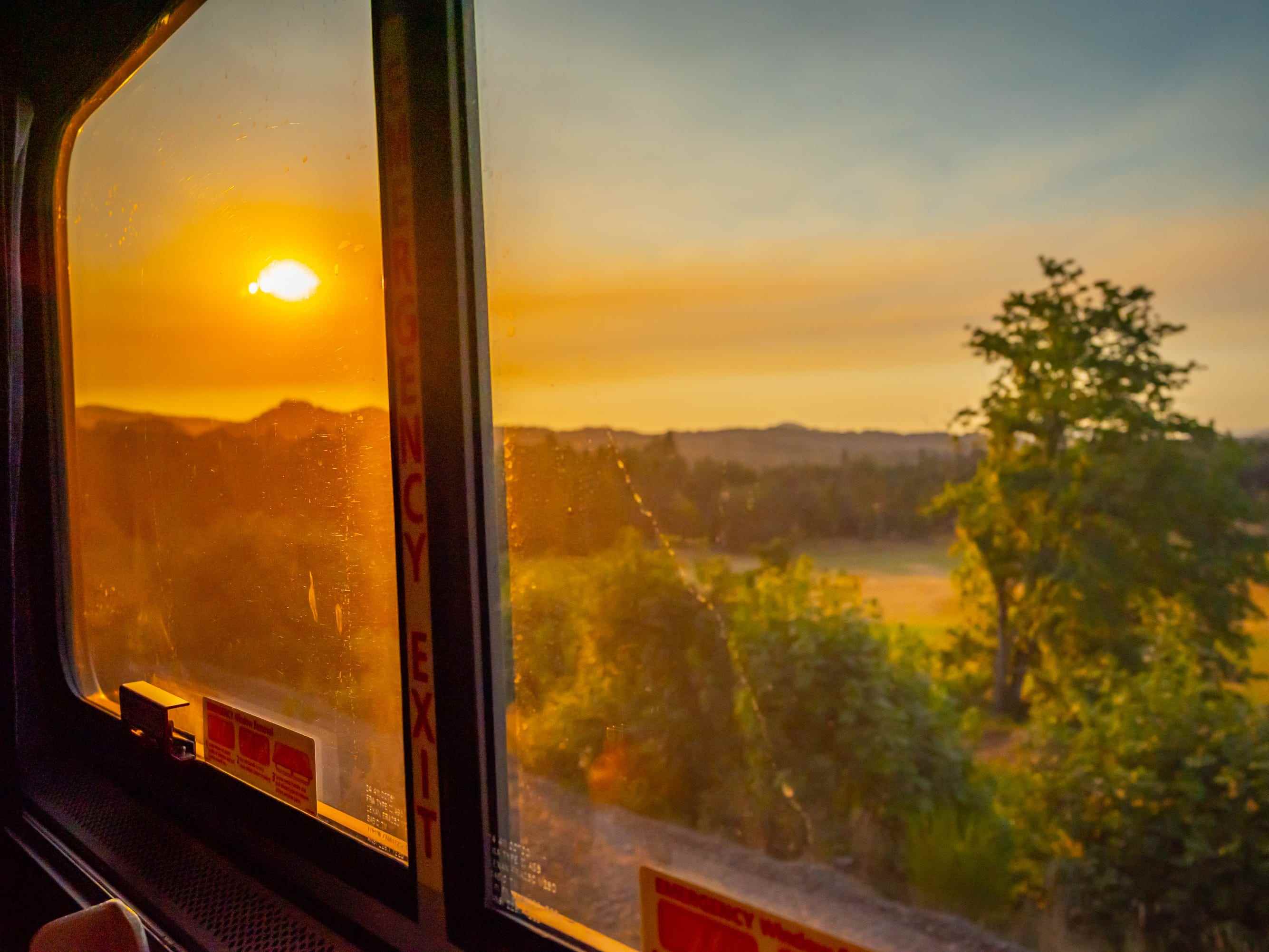 Blick auf den Sonnenuntergang vor Bergen und Bäumen außerhalb des Amtrak-Fensters