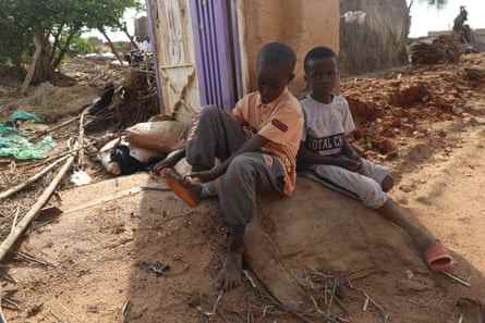 Zwei Jungen sitzen neben einem beschädigten Haus