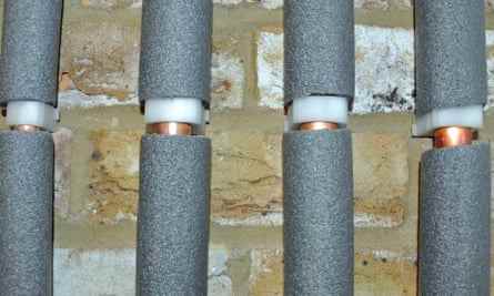 Vier Wasserleitungen in grauer Schaumisolierung gegen eine Ziegelwand.