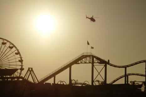 Hoch über der Achterbahn – ein Helikopter schwebt am Santa Monica Pier in den Sonnenuntergang