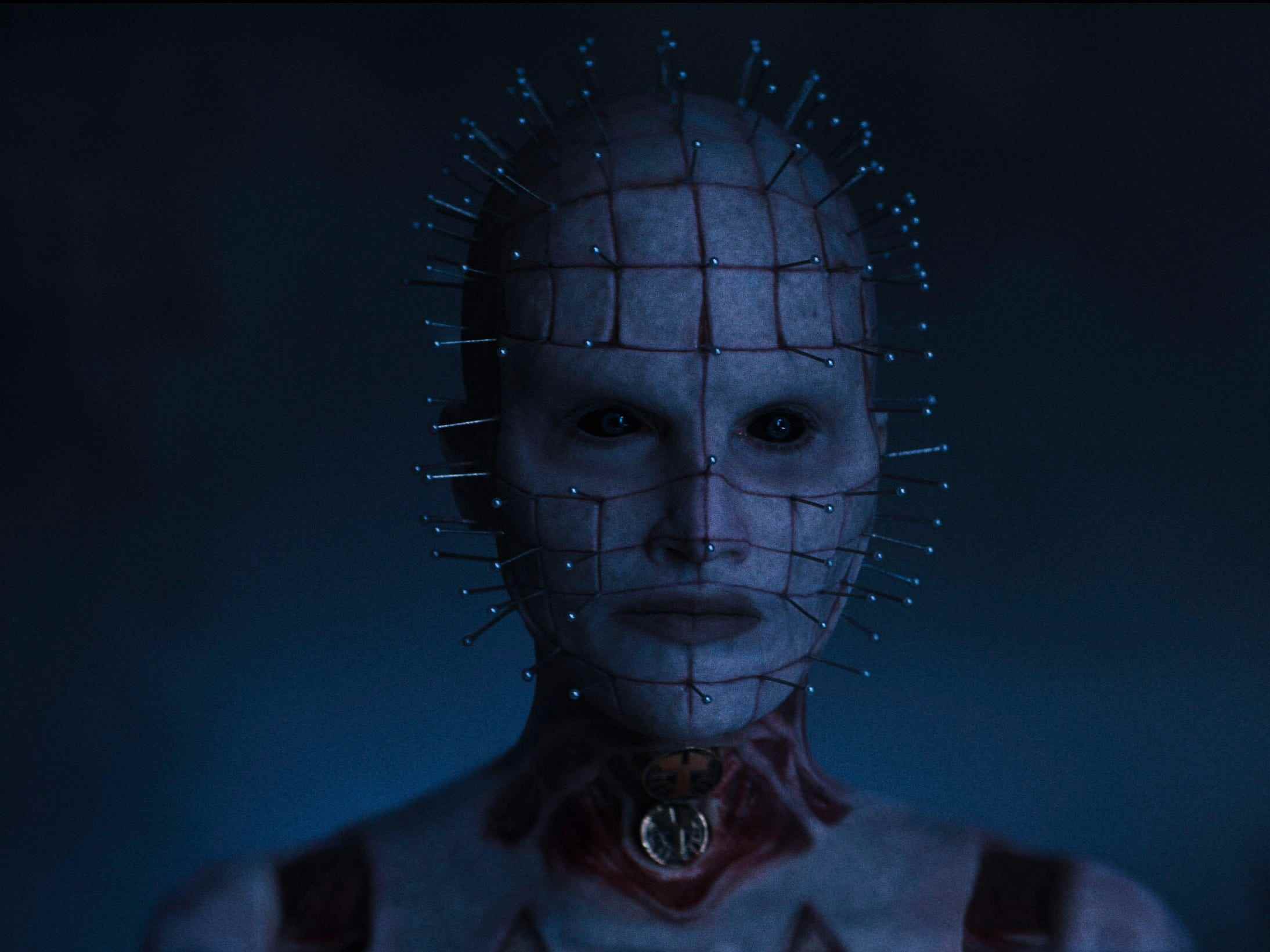 Die Figur von Pinhead, gespielt von Jamie Clayton, gezeigt in schwachem blauem Licht mit Nadeln, die aus ihrem Gesicht und Kopf ragen.