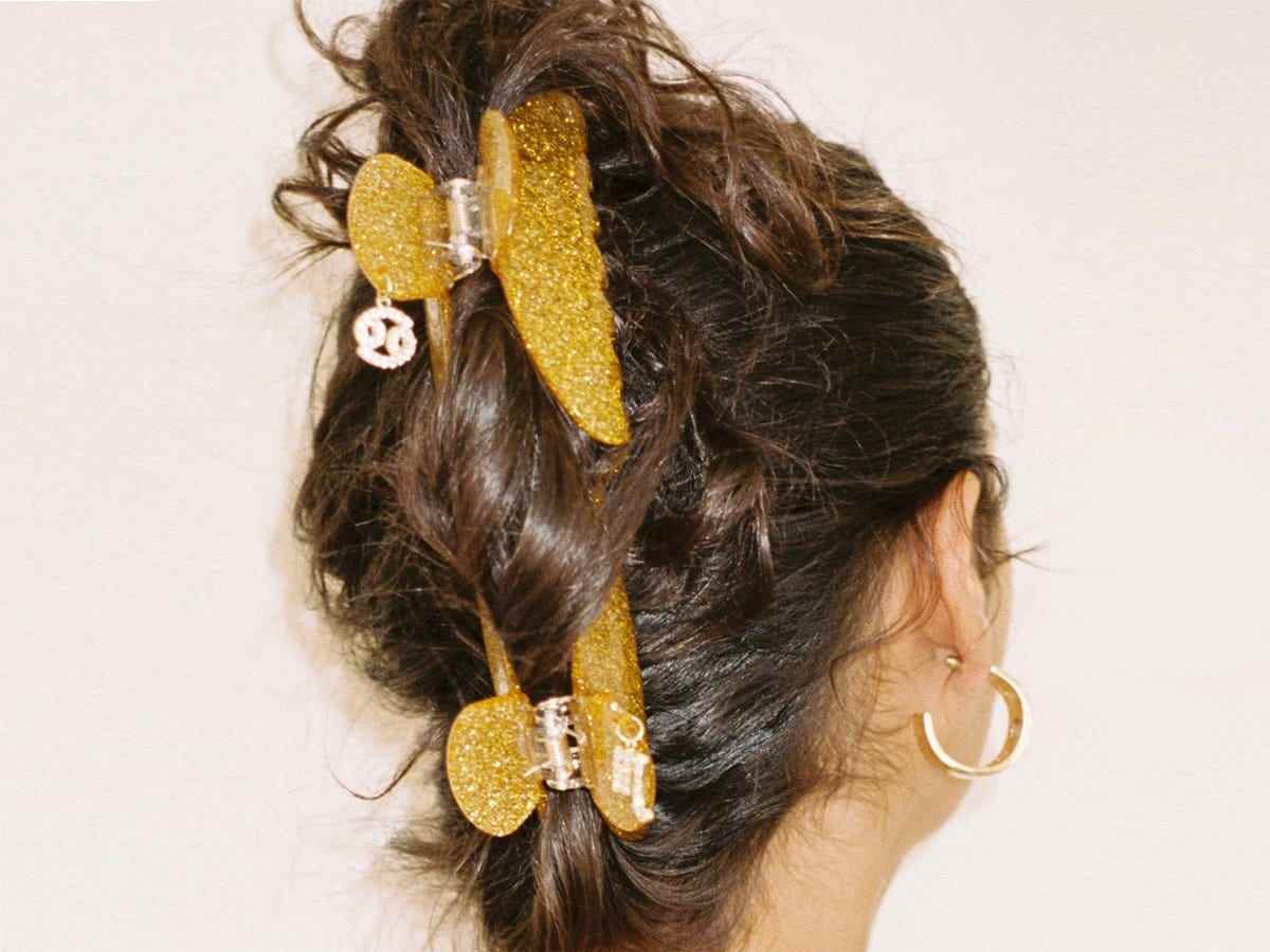Eine brünette Person, die zwei funkelnde goldene Zodiac-Klauenklammern verwendet, um ihre Haare hochzuhalten.