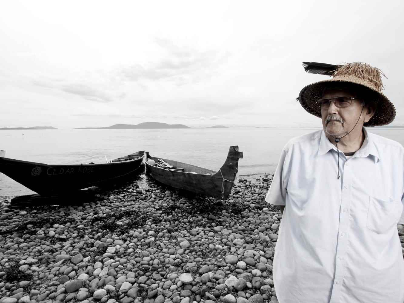 Häuptling Bill James, Lummi Nation.  Ein Mann posiert für ein Porträt vor einem Kanu und Wasser.