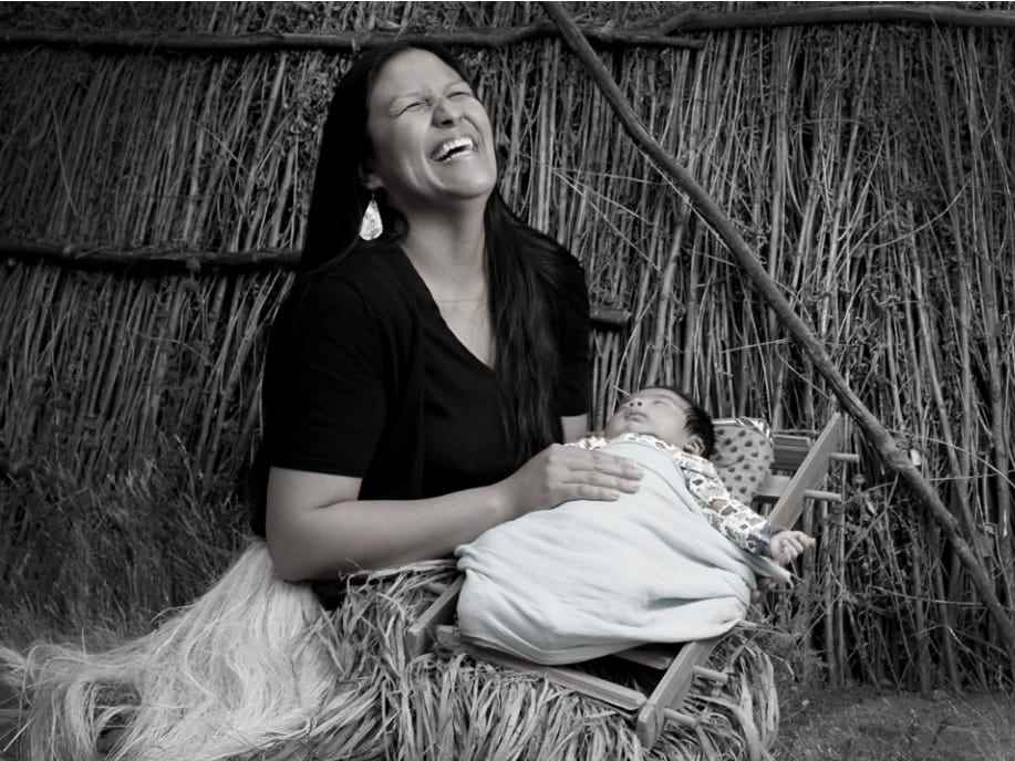 Eine indianische Frau lacht, während sie ihr Baby hält.