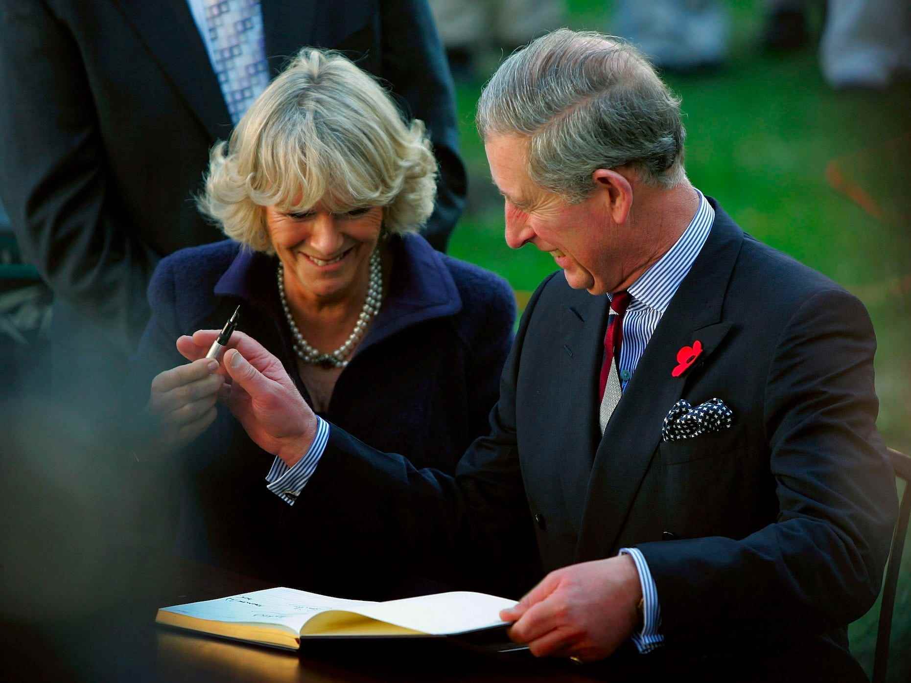 Camilla, Queen Consort und King Charles III lachen, als er ihr einen Stift reicht.