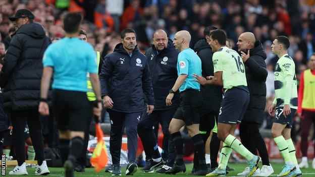 Anthony Taylor bahnt sich seinen Weg durch eine Menge Spieler und Trainer von Manchester City, um den Monitor am Spielfeldrand zu inspizieren.