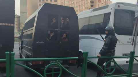 Eine Gruppe von Menschen schaut aus einem scheinbaren Sicherheitswagen in Teheran, während ein Beamter in der Nähe steht.