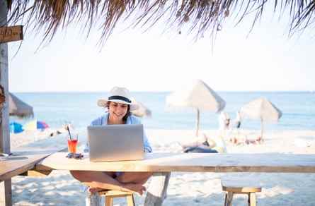 Aufnahme einer Frau, die in einem Strandcafé sitzt und einen Laptop benutzt.