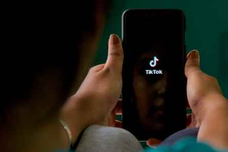 Eine Frau hält ein Smartphone mit dem TikTok-Logo auf schwarzem Hintergrund.