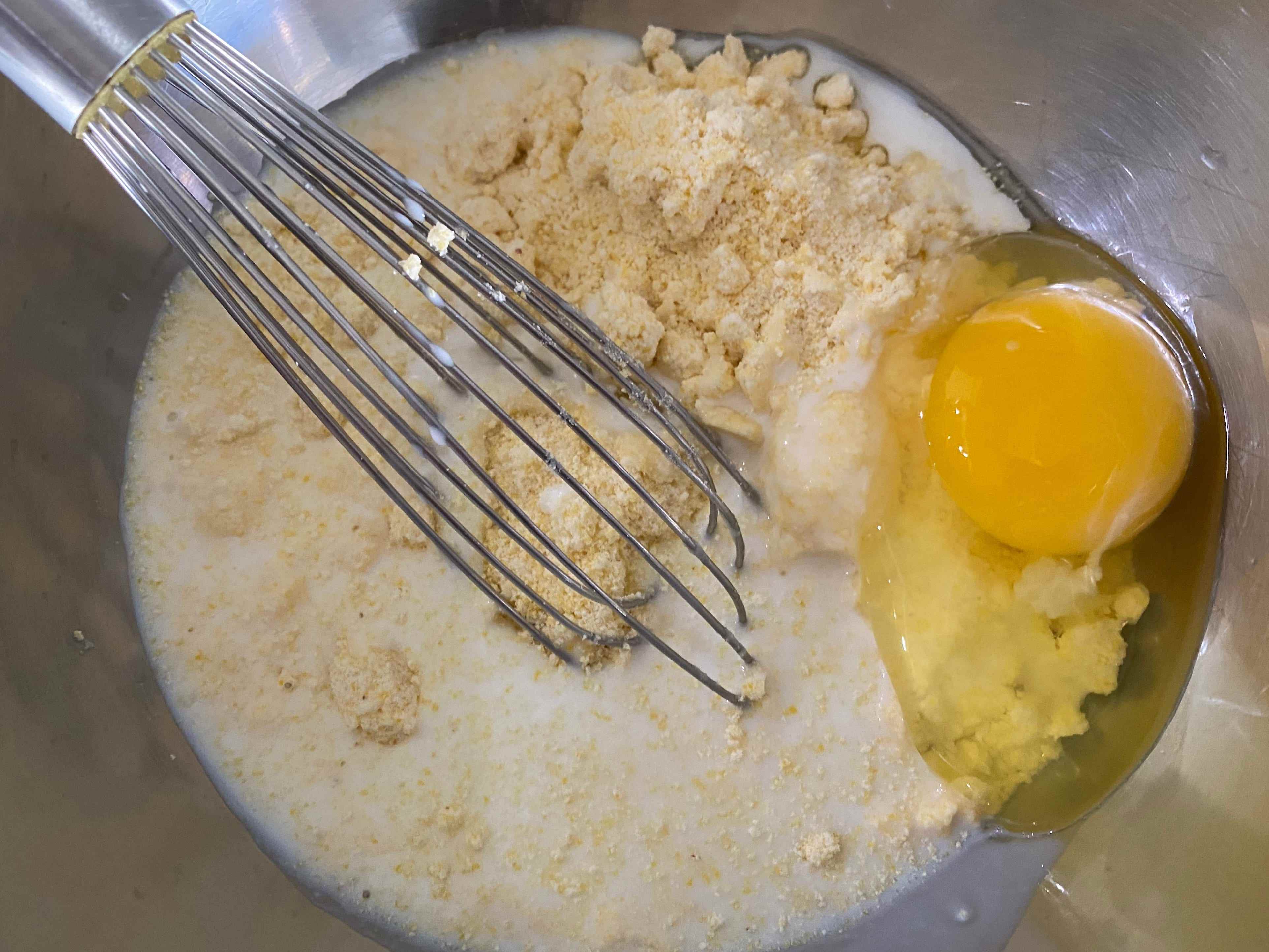 Ei in Milch in einer Schüssel mit Jiffy's Maisbrotmischung, die in einer silbernen Schüssel verquirlt wird